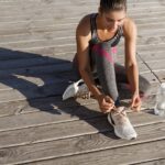 Mujer joven atándose las zapatillas de correr sentada en un paseo de madera antes de entrenar
