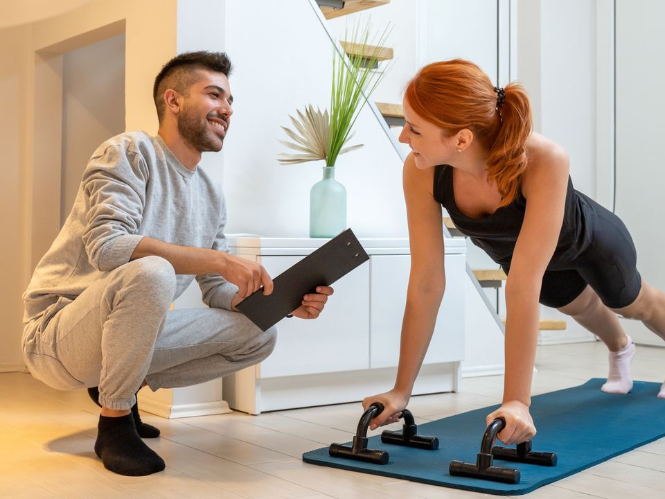 Entrenador personal con una clienta haciendo flexiones en el salón de su casa