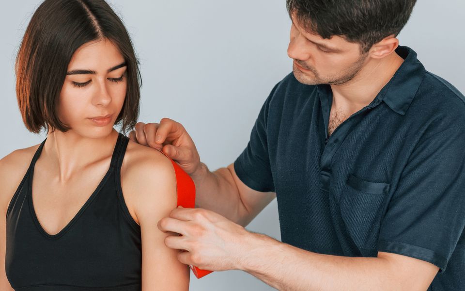 Fisioterapeuta poniendo cinta de kinesiología en el hombro de una deportista