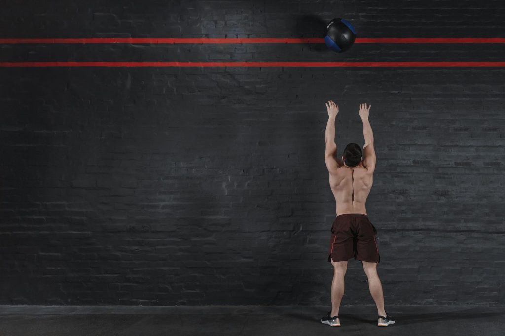 Deportista lanzando una bola contra la pared en un gimnasio, el último ejercicio de HYROX